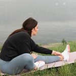 A woman stretches on a yoga mat by a serene lake, embodying relaxation and wellness in nature.